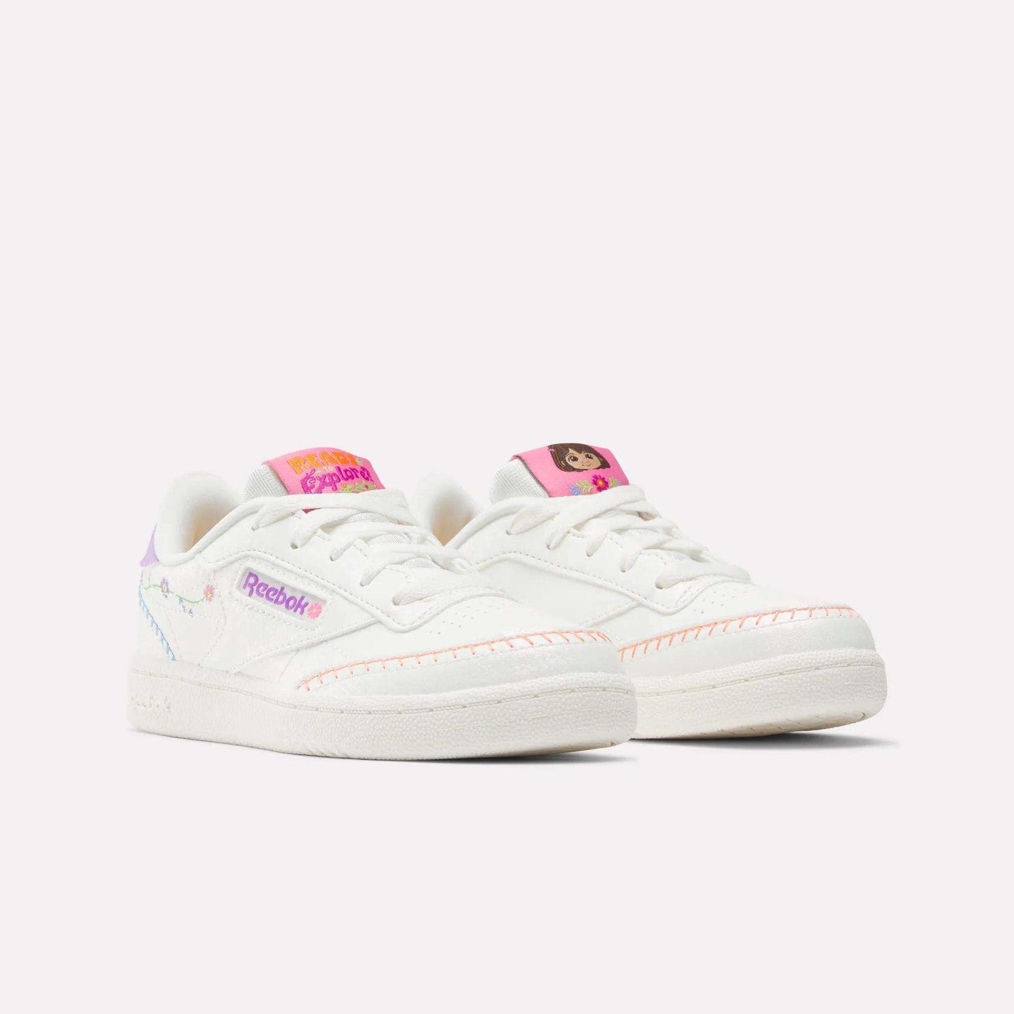 The Reebok x DORA Club C Shoes for little kids feature playful Dora the Explorer designs, white uppers with pink accents, and colorful side details for a fun look.