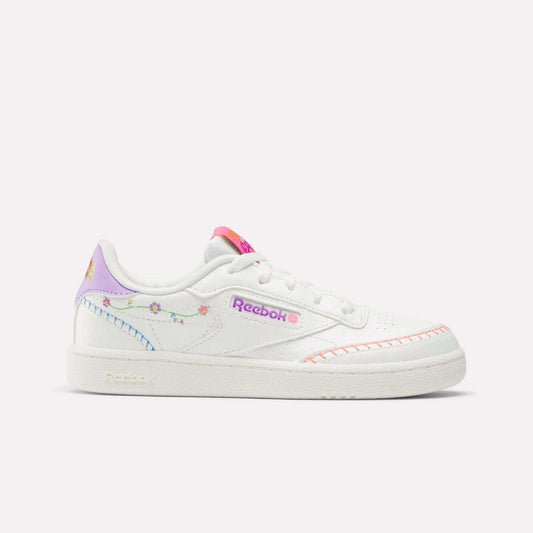 The Reebok x DORA Club C Shoes for little kids feature pastel rainbow accents, floral embroidery, a pink logo, and orange stitching on white—perfect colorful shoes by Reebok for playful style.