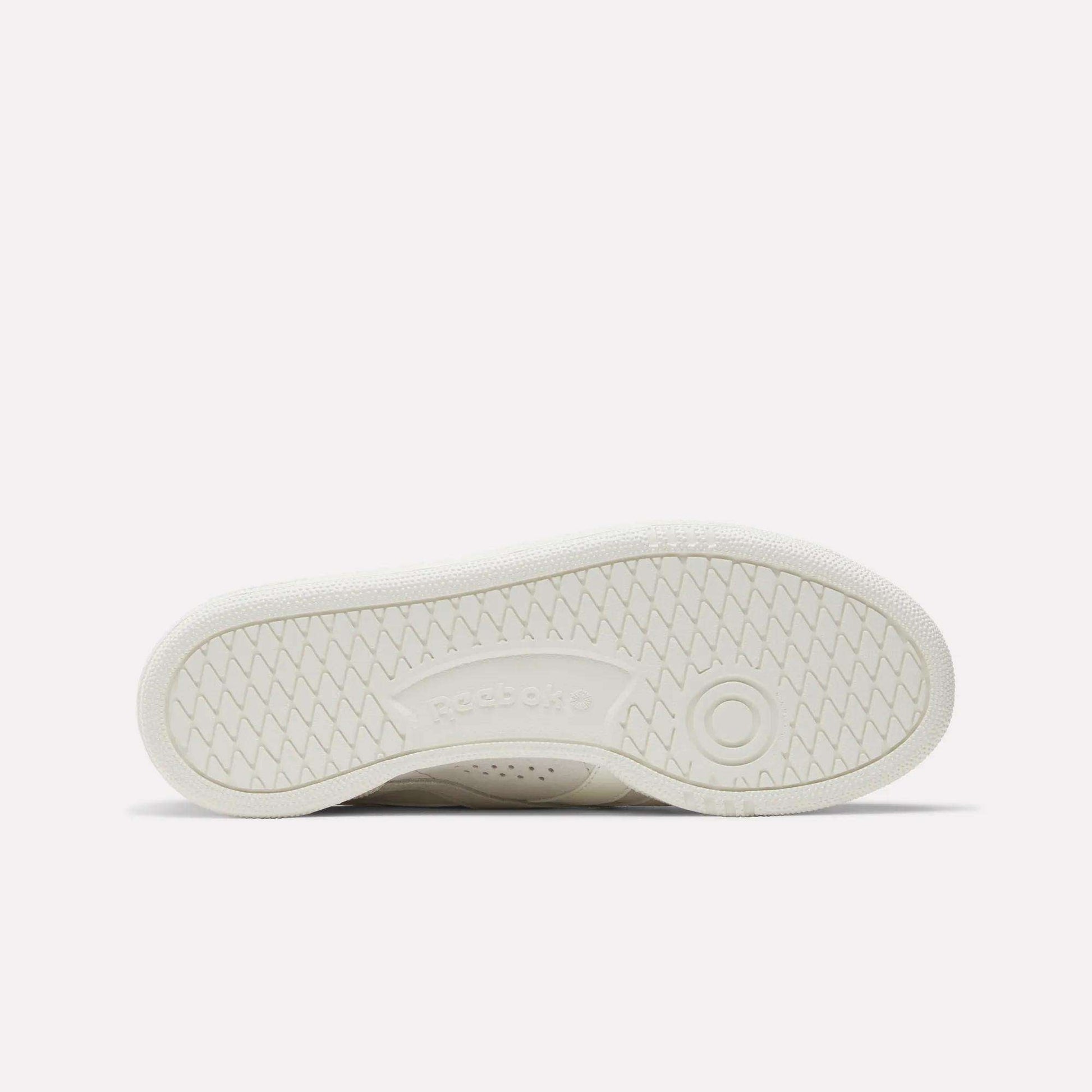 The image shows the white sole of the Reebok Women's Club C Grounds UK Shoes lying flat, with a herringbone tread pattern and an embossed Reebok logo at the center.