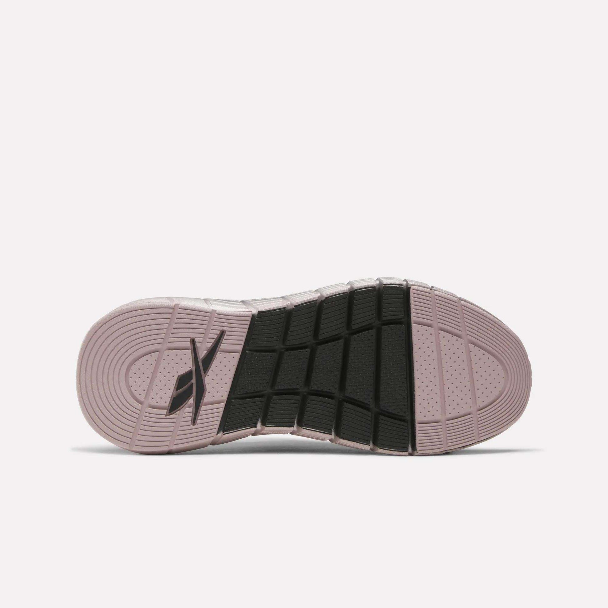 The image shows the sole of Reebok Women's Nano Gym Training Shoes with a pinkish outer edge, black rectangular grips in the center, a logo near the heel, and features concentric circles and textured patterns for traction.