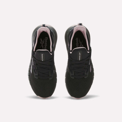 A pair of Reebok Women's Nano Gym Training Shoes in black with white soles and pink accents, shown from above on a white background. Versatile for workouts, they feature the Reebok logo on the insoles.