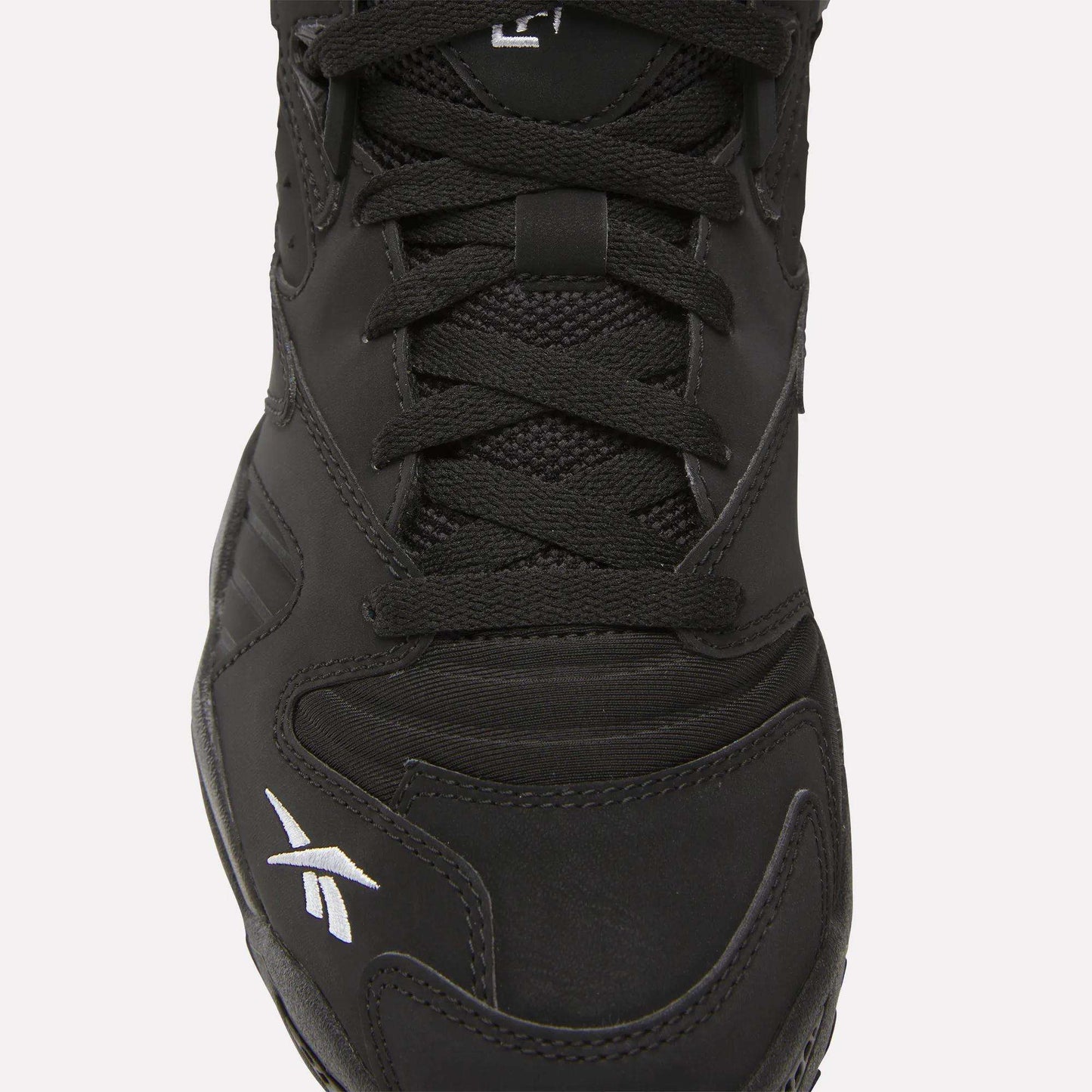 Close-up of the Brutus Low Shoes by Reebok in black, featuring black laces, mesh and leather upper, and a white logo on the toe—perfect for adding street-ready style to your look.