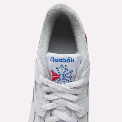 Top view of Reebok Women's Workout Plus Shoes in white, featuring white laces, grey lining, and a blue Reebok logo with red and blue starburst on the tongue—classic '80s fitness style.