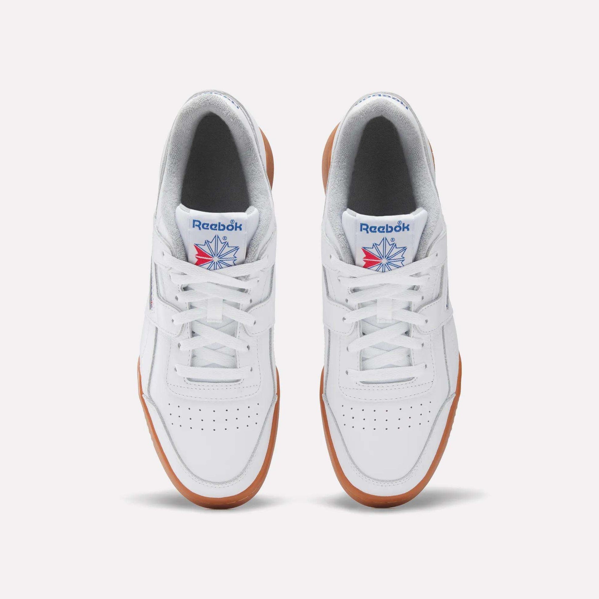 Top view of the Reebok Women's Workout Plus Shoes: classic white sneakers with brown gum soles, perforated toes, blue and red Reebok logos on the tongues, and a subtle '80s fitness vibe.