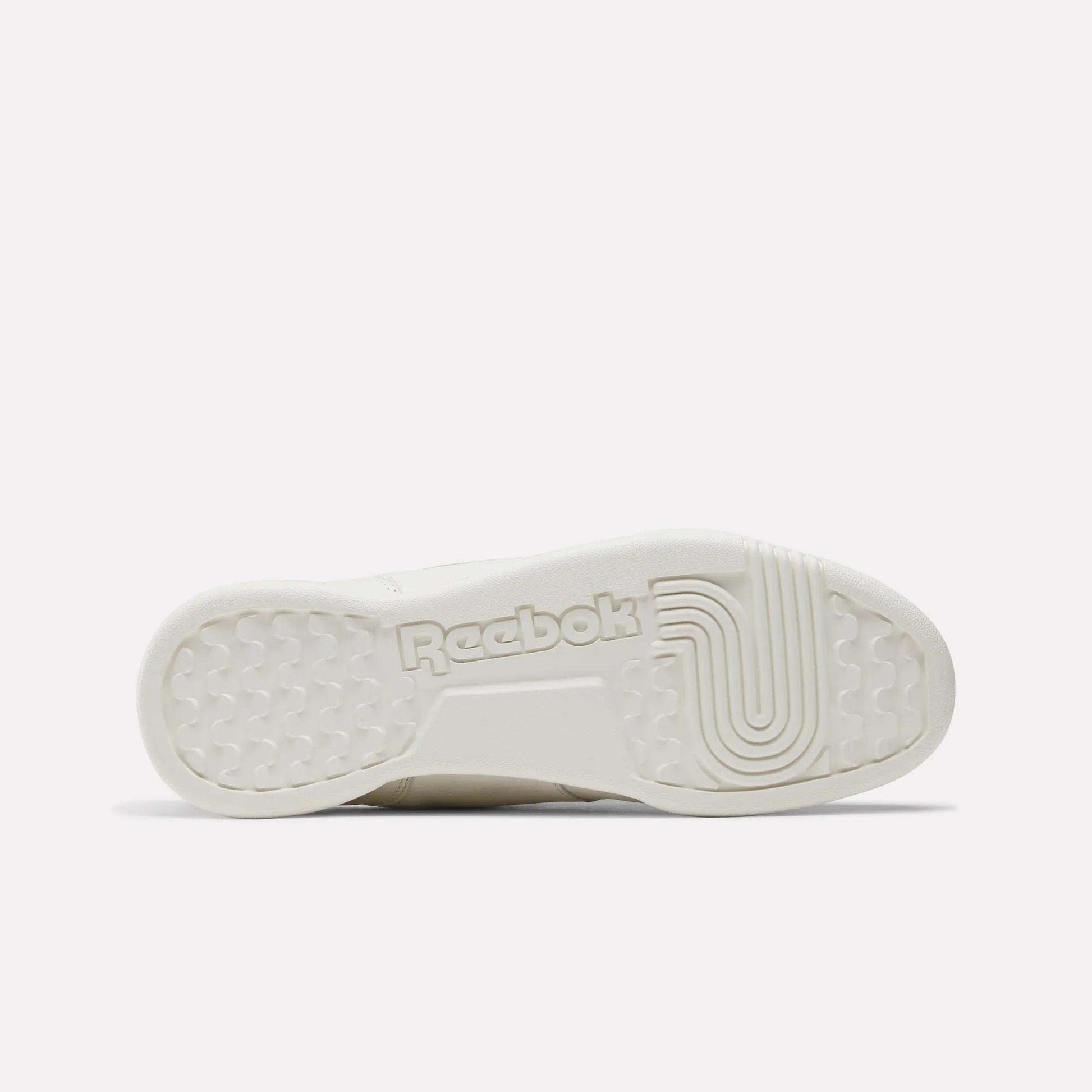 The image displays the sole of Reebok Women's Workout Plus Shoes, featuring the Reebok branding and a mix of circular and linear tread patterns for optimal grip—perfect for women seeking versatile workout footwear.