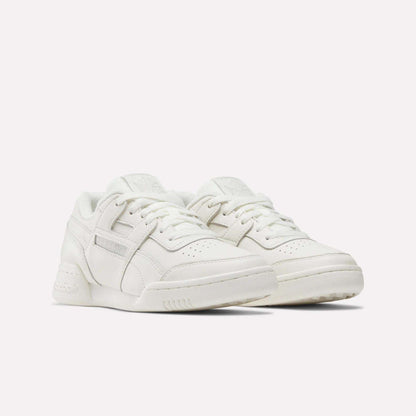 A pair of Women's Workout Plus Shoes by Reebok, featuring a white low-top design with laces, perforated toe boxes, and subtle stitching details, displayed against a plain white background.