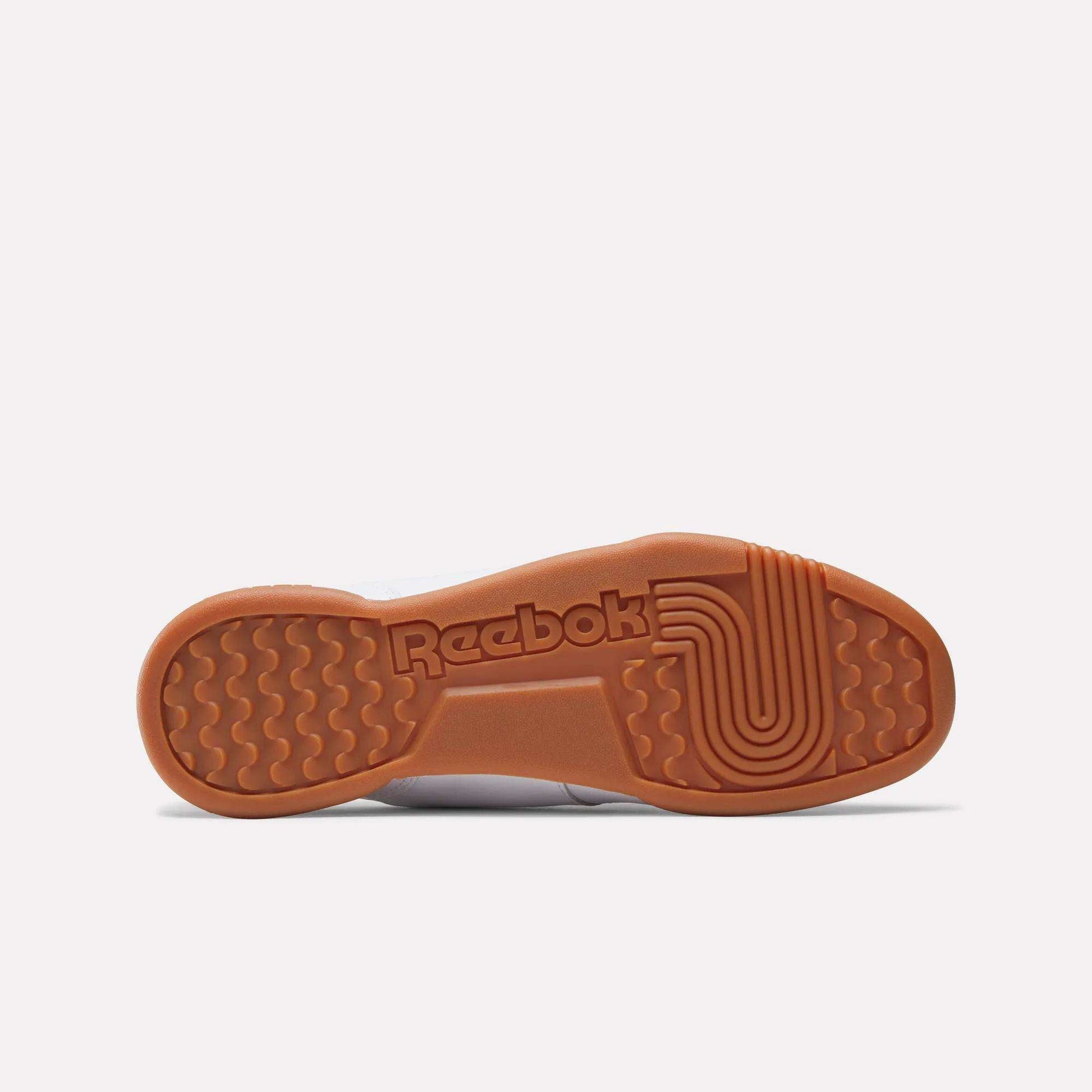 Bottom view of the Reebok Workout Plus Shoes with a brown rubber sole, textured grip patterns, and the embossed Reebok logo at the center—showcasing iconic '80s fitness-inspired style.