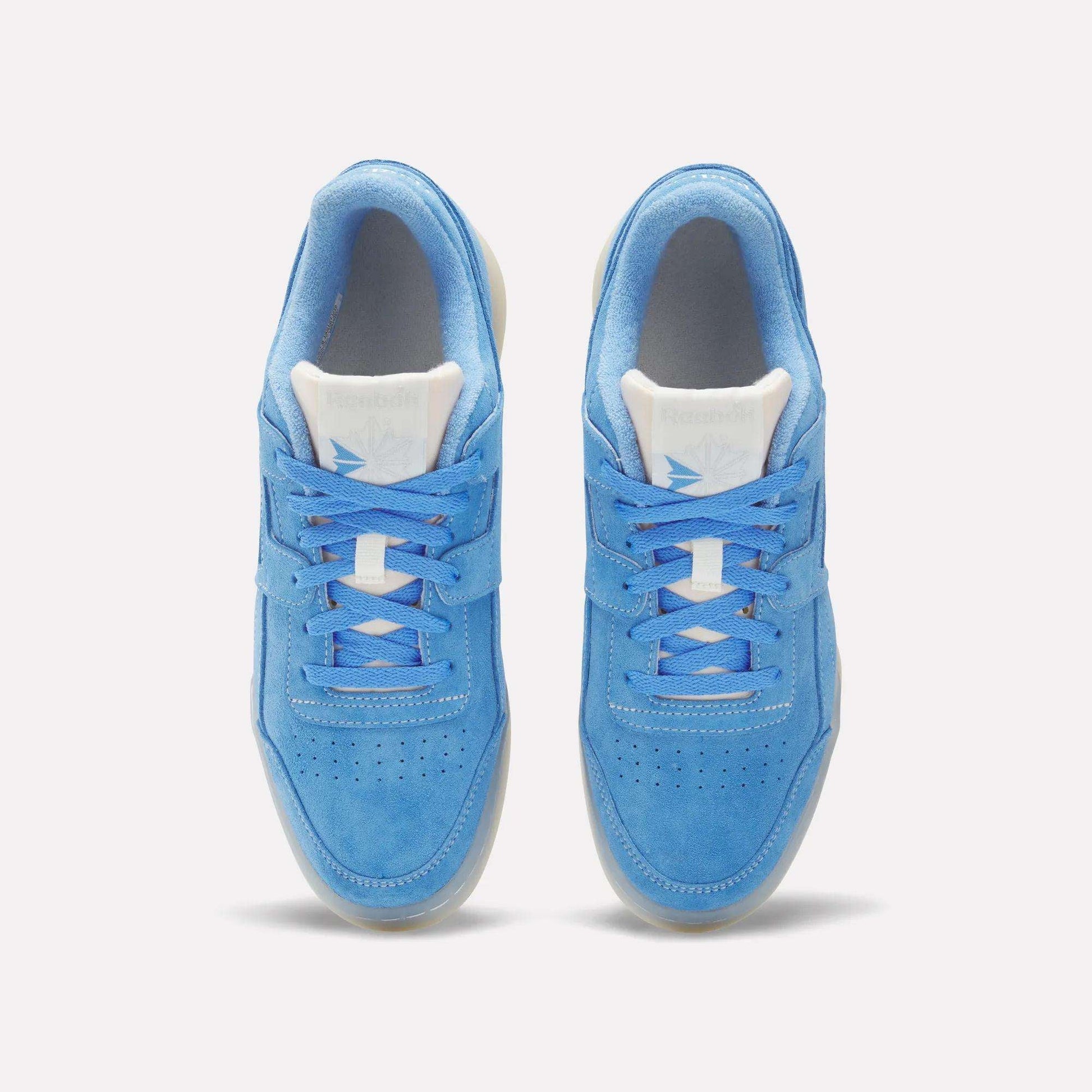 A pair of Reebok Workout Plus Shoes in light blue suede, with white tongues and laces, seen from above on a neutral background. Perforated toe boxes and classic '80s fitness style complete the retro look.
