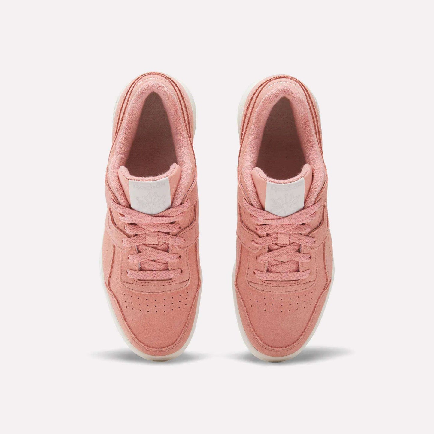 A pair of Women's Workout Plus Shoes by Reebok in pink with white soles, top view highlighting laces, perforated toes, and a white logo patch on the tongue—ideal for capturing vintage 80s workout style.
