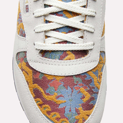Close-up of Reebok Classic Leather 1983 Vintage Shoes with white laces, light suede trim, and a colorful yellow, blue, and red floral pattern. A small British flag patch near the laces adds to the retro look.