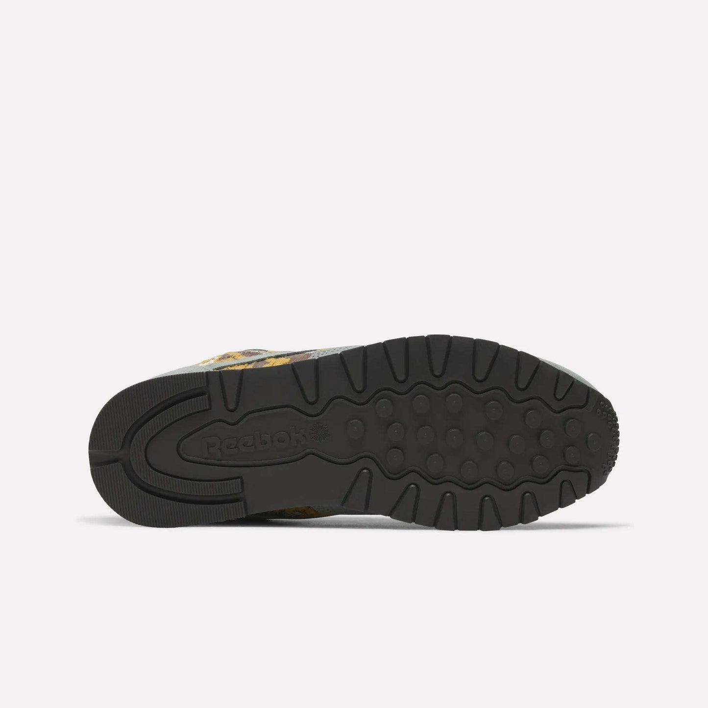 The image displays the underside of Reebok’s Classic Leather 1983 Vintage Shoes, featuring a black rubber sole with textured grip patterns and an embossed Reebok logo near the heel against a plain, light-colored background.