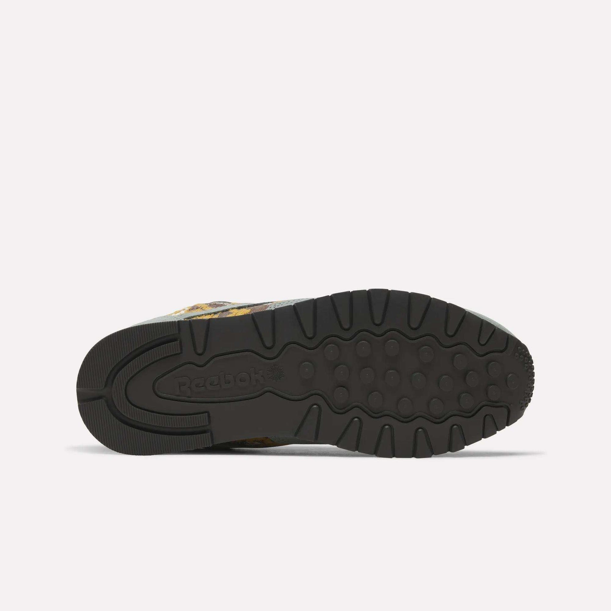 The image displays the underside of Reebok’s Classic Leather 1983 Vintage Shoes, featuring a black rubber sole with textured grip patterns and an embossed Reebok logo near the heel against a plain, light-colored background.
