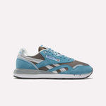 The Reebok Classic Nylon 89 Shoes feature blue suede, silver accents, and gray mesh panels, plus a cushioned midsole for comfort. Blue laces and a white-gray sole complete the vintage running look on a plain white background.