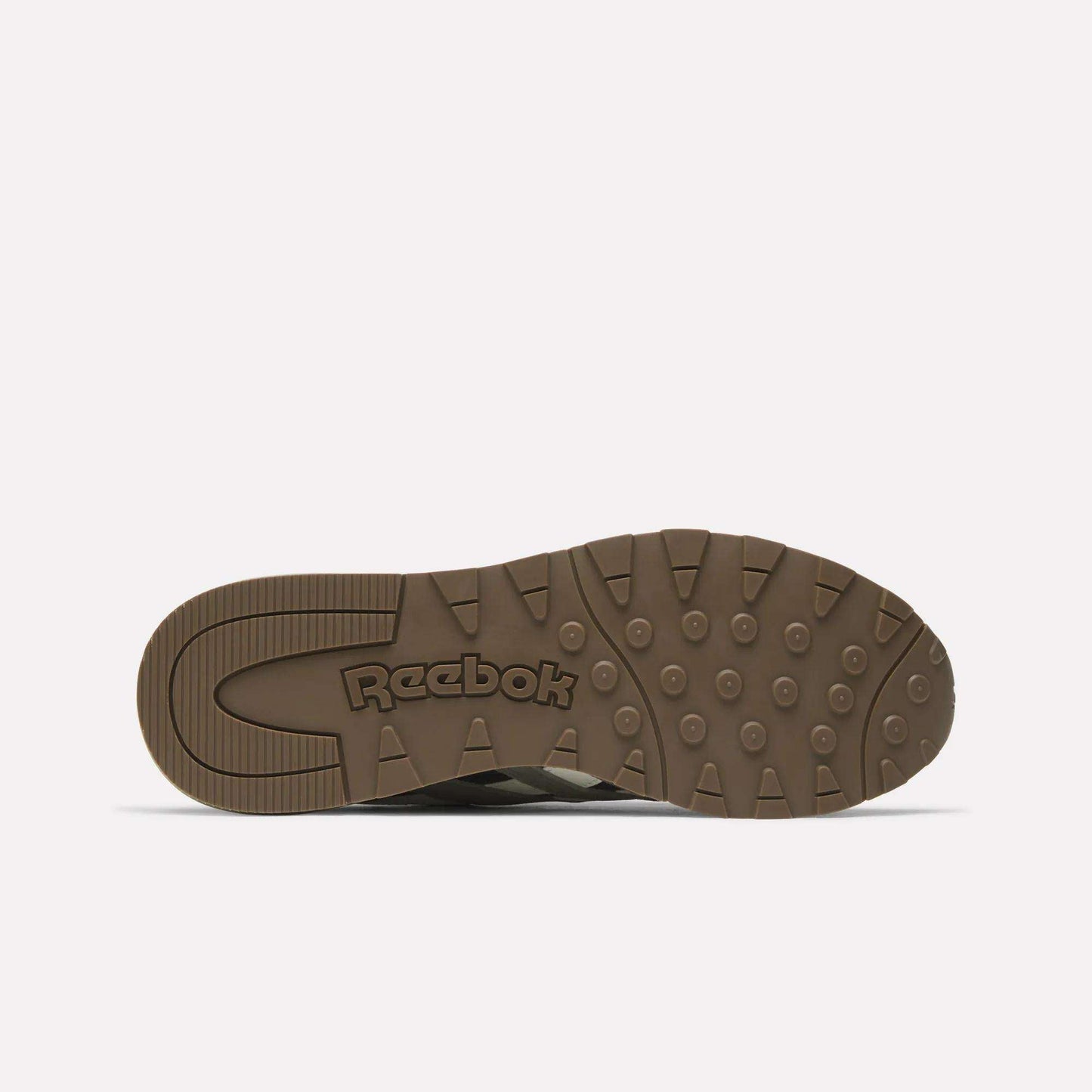 The image shows the bottom view of a brown Classic Nylon 89 Shoes sole by Reebok, featuring circular and rectangular grip patterns with the Reebok logo embossed in the center.