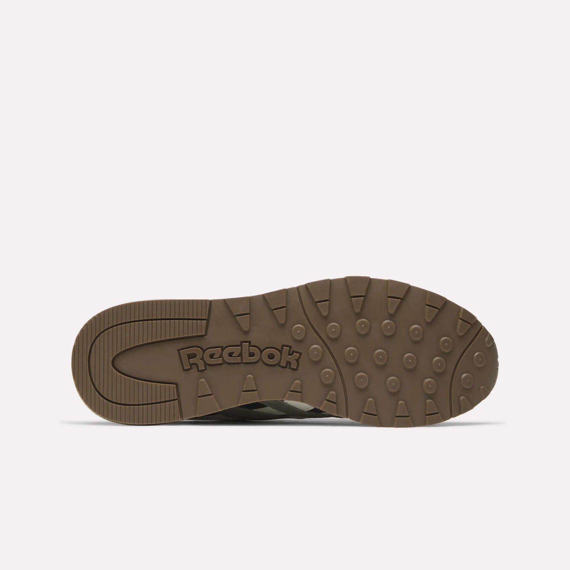 The image shows the bottom view of a brown Classic Nylon 89 Shoes sole by Reebok, featuring circular and rectangular grip patterns with the Reebok logo embossed in the center.