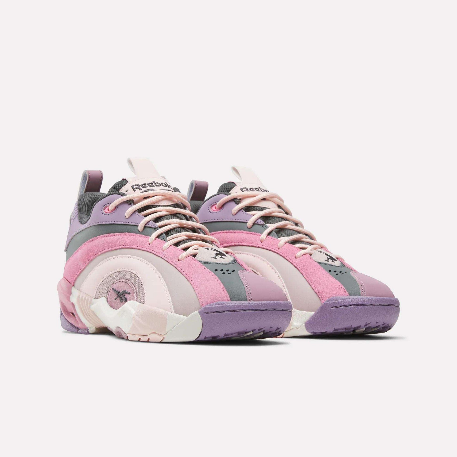 The Reebok Shaqnosis Low Shoes, shown against a plain white background, feature wavy design lines and Hexalite cushioning in shades of pink, purple, and gray with cream accents.
