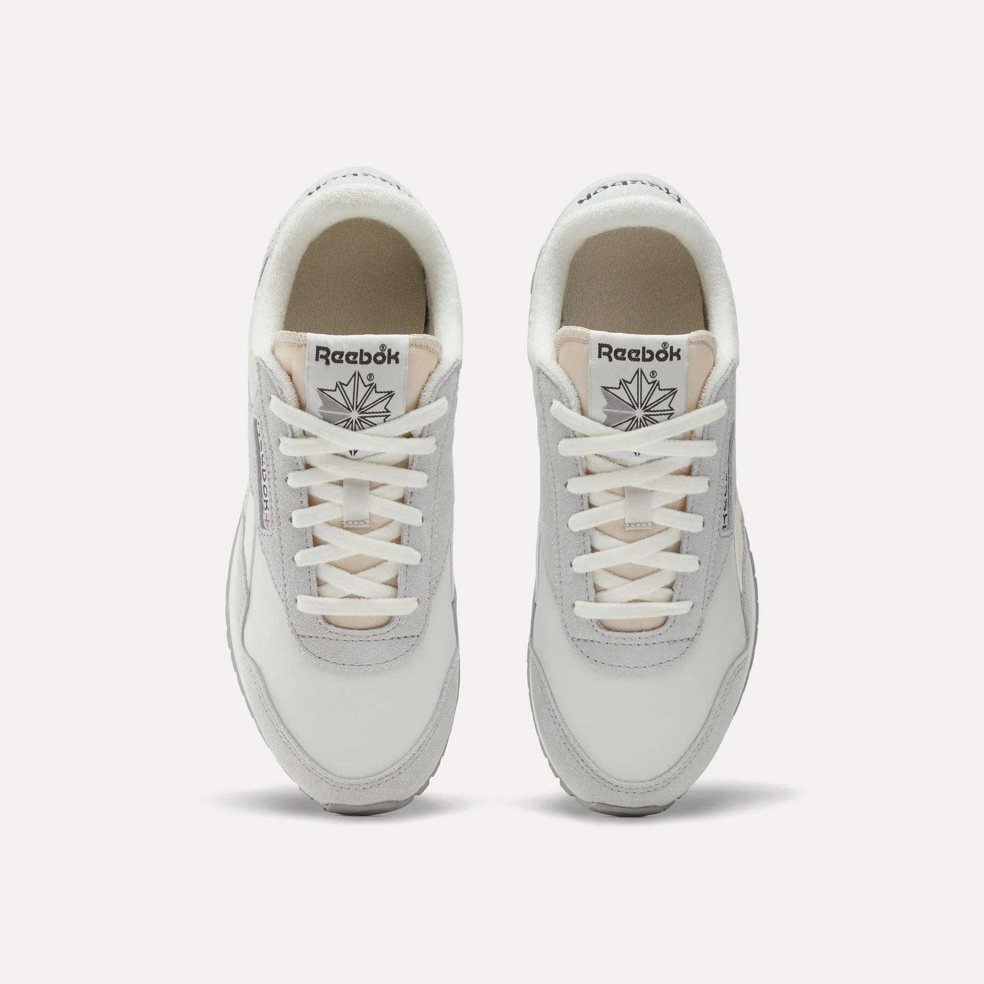Top view of a pair of Women's Classic AZ Shoes by Reebok in white and light gray with white laces, low-profile design, and the Reebok logo visible on each tongue, displayed side by side on a plain background.