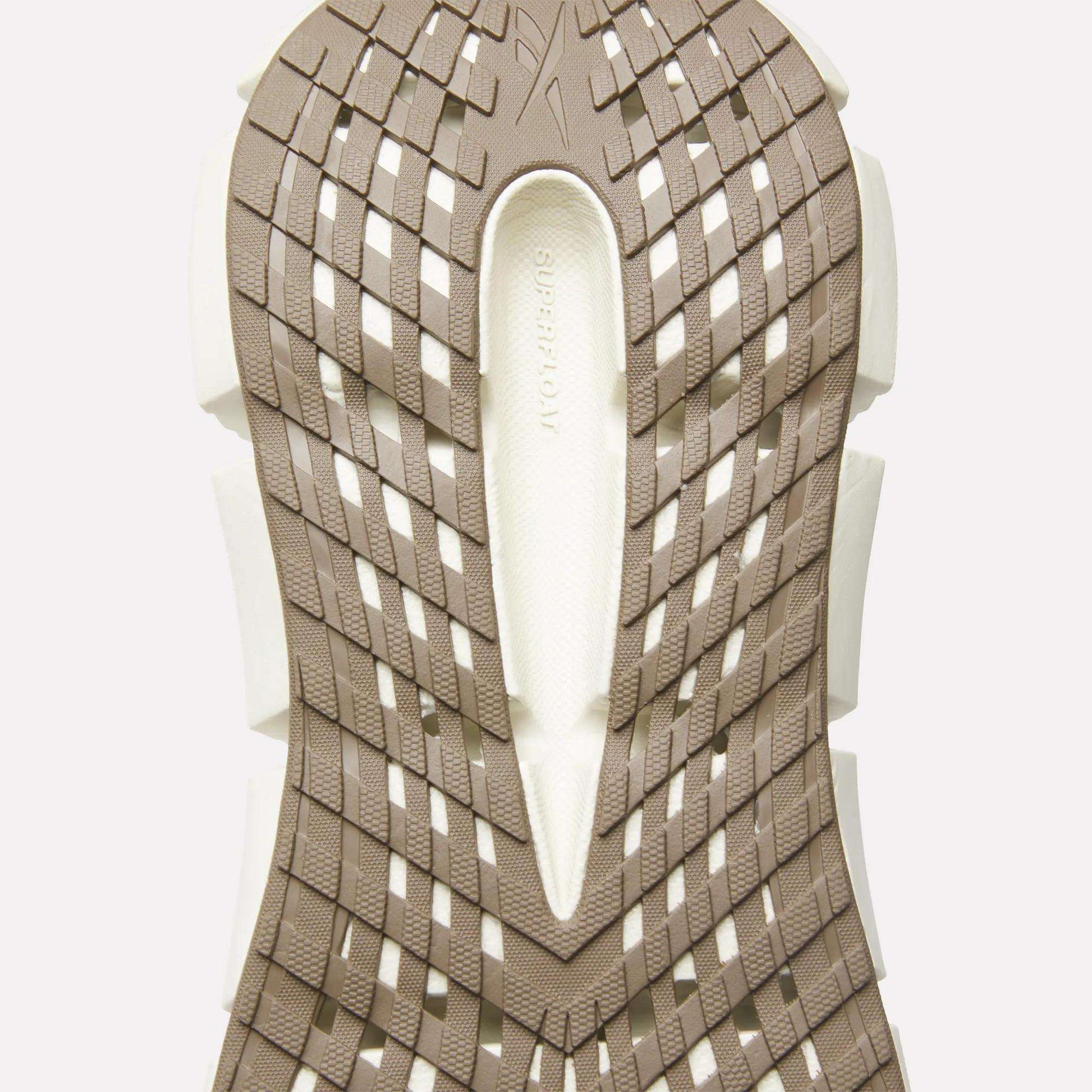 Close-up of the beige and white sole on Reebok Men's FloatZig 2 Running Shoes, showcasing a geometric crisscross tread with 'SUPERFLOW' embossed in the center, highlighting Superfloat+ cushioning for enhanced comfort.