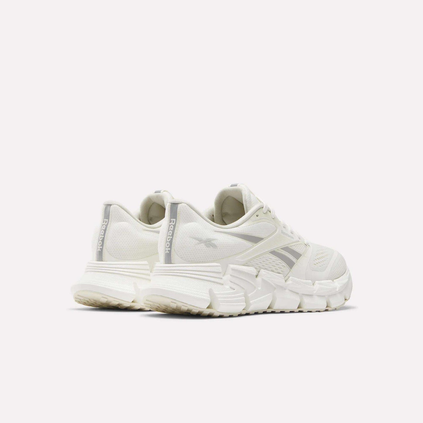 The Reebok Women's FloatZig 2 Running Shoes in white are shown from the back and side against a plain light background, emphasizing the chunky energy-returning cushioning and prominent Reebok branding on the heel and side.