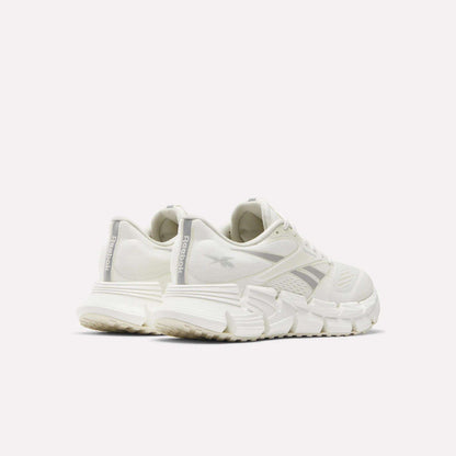 The Reebok Women's FloatZig 2 Running Shoes in white are shown from the back and side against a plain light background, emphasizing the chunky energy-returning cushioning and prominent Reebok branding on the heel and side.