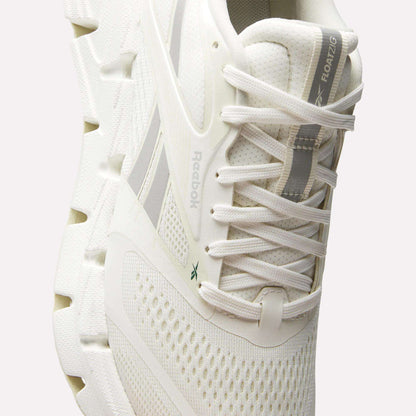 A close-up of the Reebok Women's FloatZig 2 Running Shoes, showing white textured mesh, a thick segmented energy-returning sole, lace-up design, subtle grey accents, and FLOATZIG branding on the tongue.
