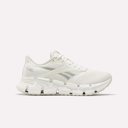 Side view of a white Reebok Women's FloatZig 2 Running Shoe featuring a mesh upper, unique angular outsole, and energy-return cushioning for comfort.
