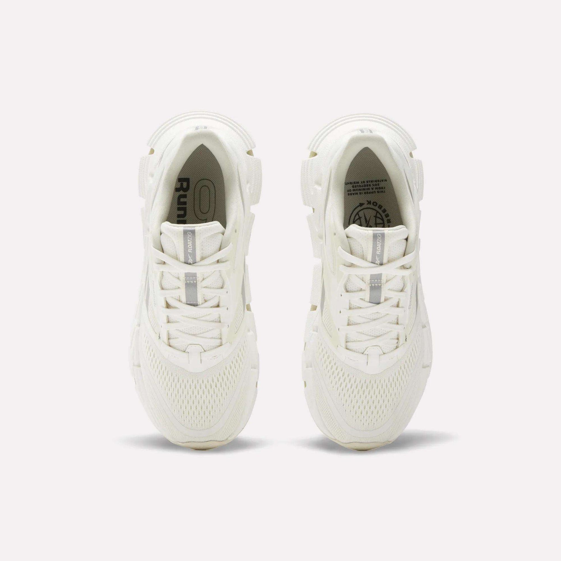 A pair of women's Reebok FloatZig 2 running shoes in white, seen from above, showcase mesh uppers, laces, and subtle Reebok branding on the insoles and tongue, with energy-returning cushioning against a plain light background.