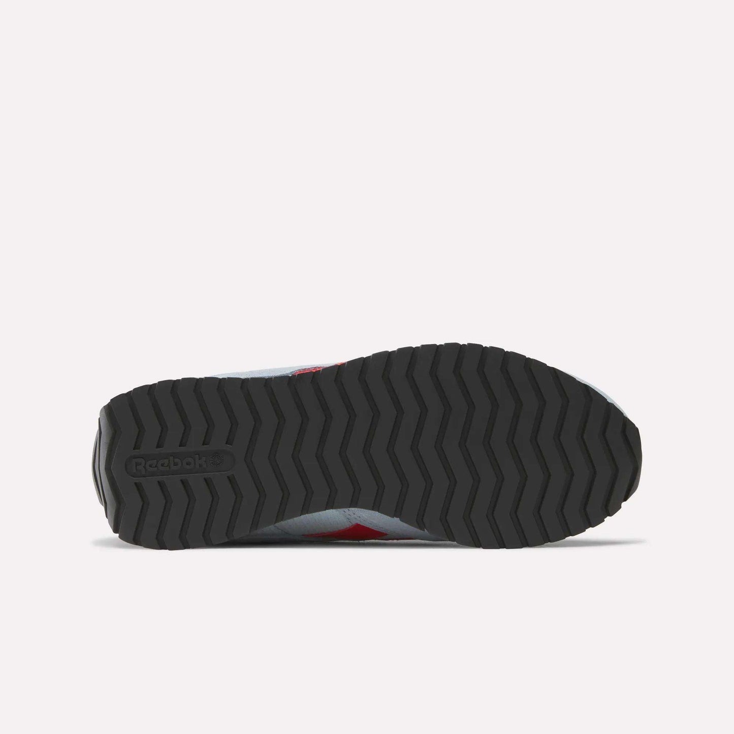 The image shows the bottom view of a Reebok Women's Classic AZ Shoes sneaker, featuring a black zigzag rubber sole with the Reebok logo on the heel. The upper edges are visible, reflecting classic retro running style.
