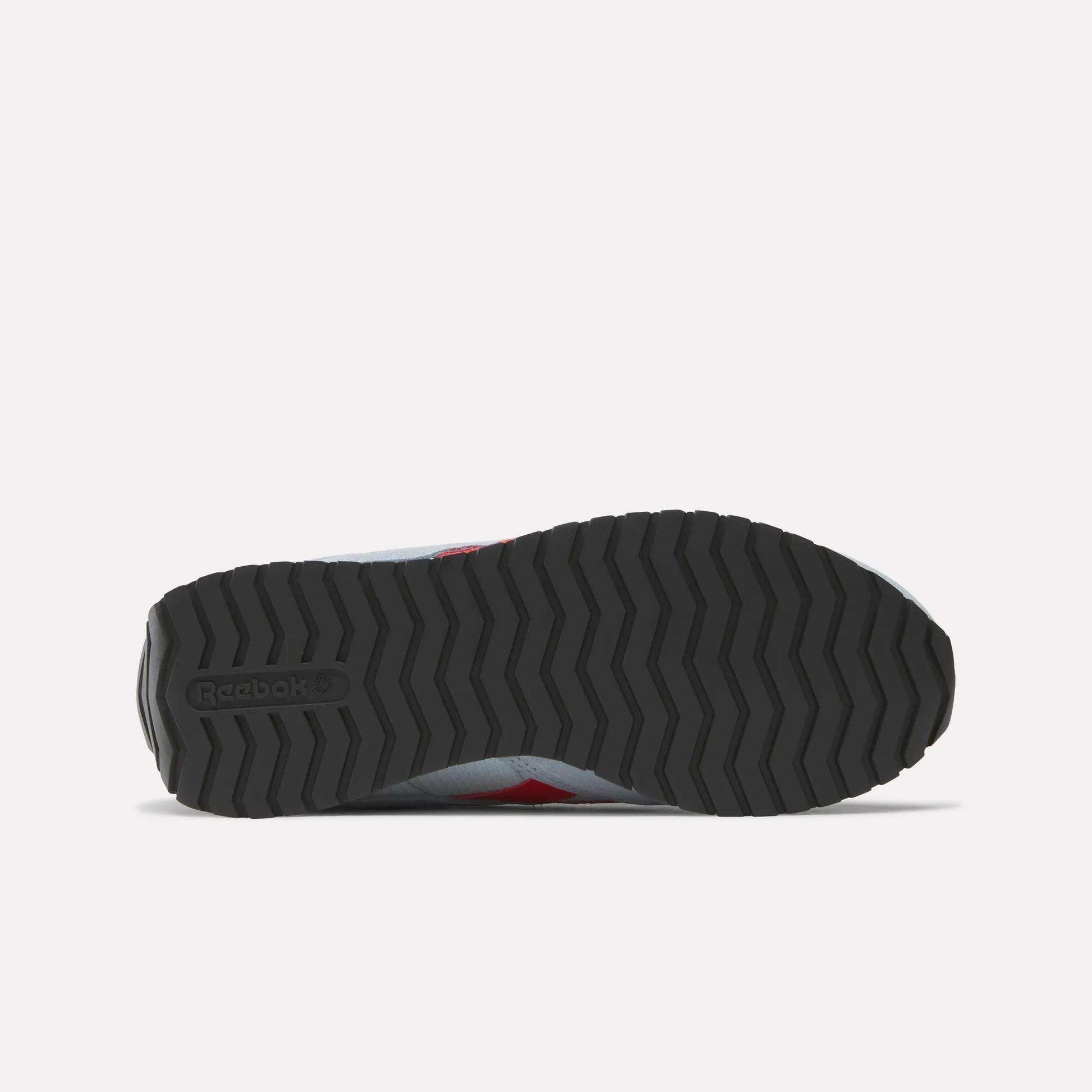 The image shows the bottom view of a Reebok Women's Classic AZ Shoes sneaker, featuring a black zigzag rubber sole with the Reebok logo on the heel. The upper edges are visible, reflecting classic retro running style.