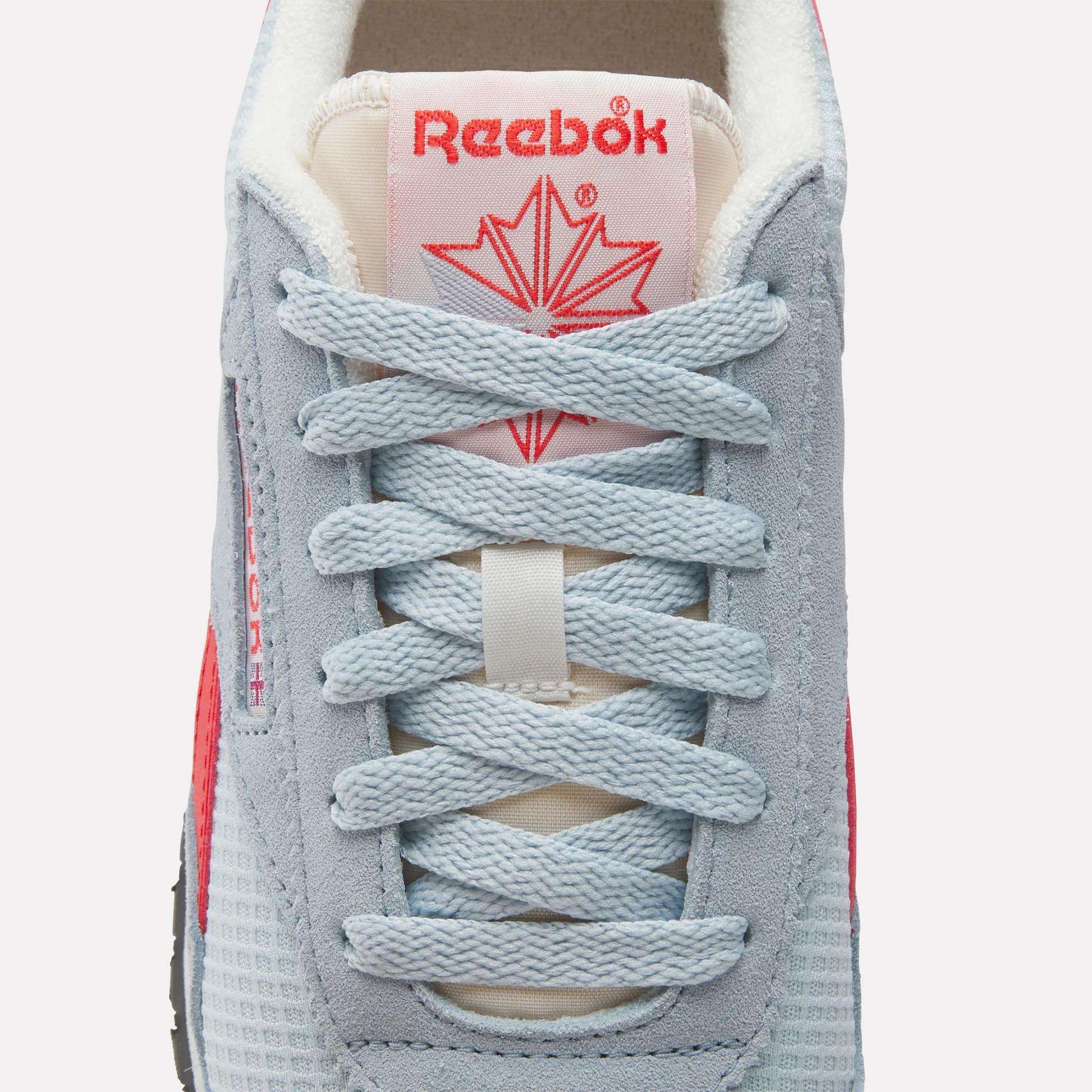 Close-up of Reebok Women's Classic AZ Shoes sneaker with light blue laces, grey and blue mesh, a red star logo on the tongue, and a hint of red on the sides—combining retro running style with modern comfort.