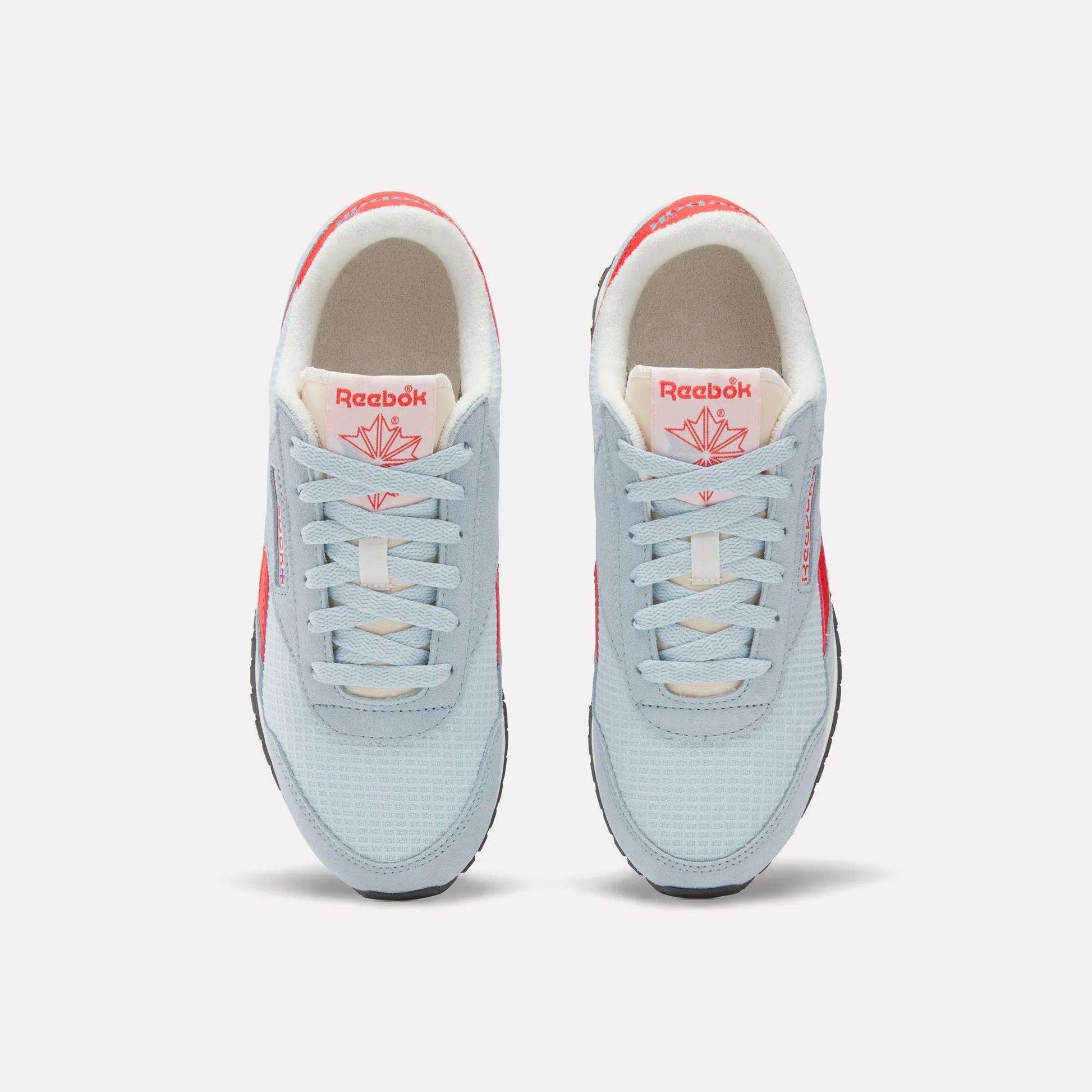 A pair of Women's Classic AZ Shoes by Reebok seen from above, with light blue uppers, white laces, beige interiors, and bright pink Reebok logos—retro running-inspired style with fresh pops of color.