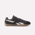 The Women's Ultra Lo Shoes by Reebok feature a black design with signature white Reebok stripes, black laces, and a light brown gum sole. This low-profile sneaker offers sport-inspired style for women. Shown in side view on a plain white background.