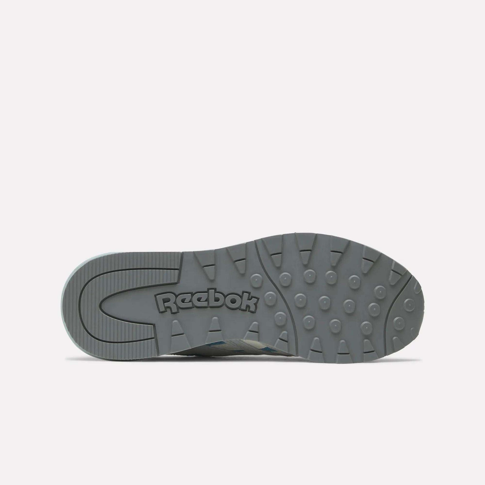 The sole of a gray Reebok Women's Classic Nylon 89 Shoe is shown from the bottom, featuring the Reebok logo and textured tread with circular grips on a white background—ideal for fans of retro style women’s running shoes.