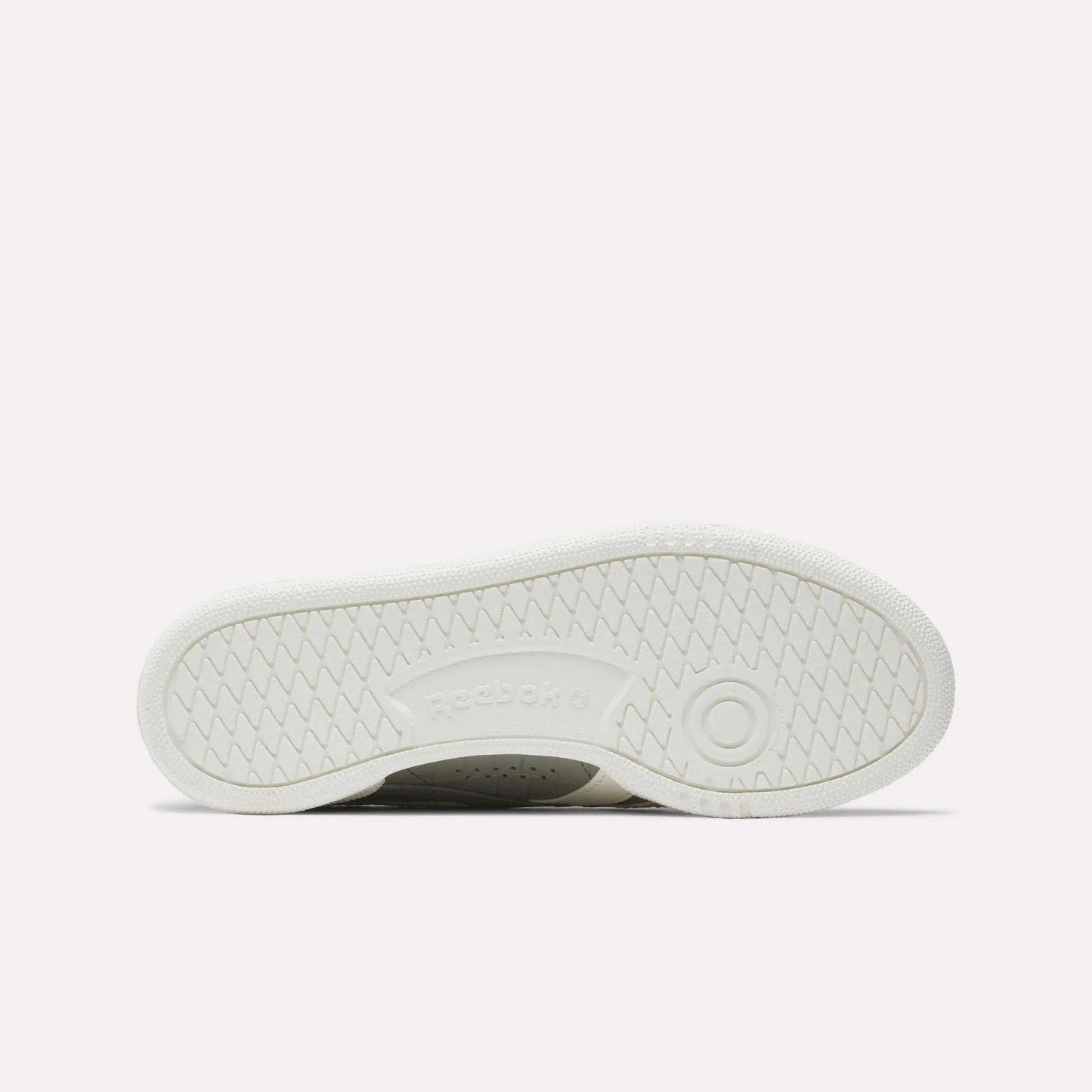 The image displays the white rubber outsole of Reebok Women's Club C Grounds UK Shoes, with a circular tread near the heel, herringbone traction patterns, and an embossed Reebok logo at the center.