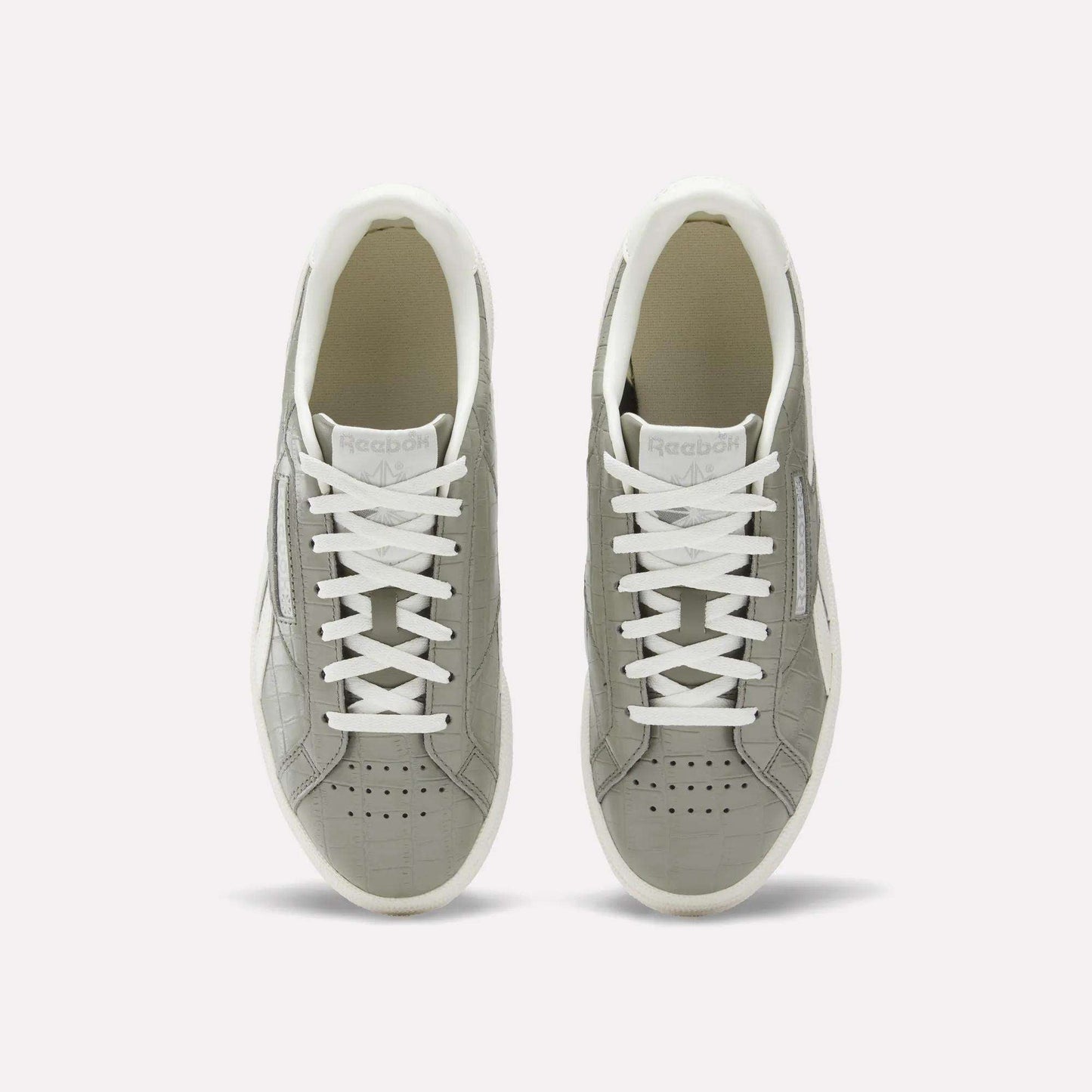 A pair of Reebok Women's Club C Grounds UK shoes in grey with white laces and soles, shown from above on a plain white background. These court-inspired shoes have perforated toes and a clean white inner lining.