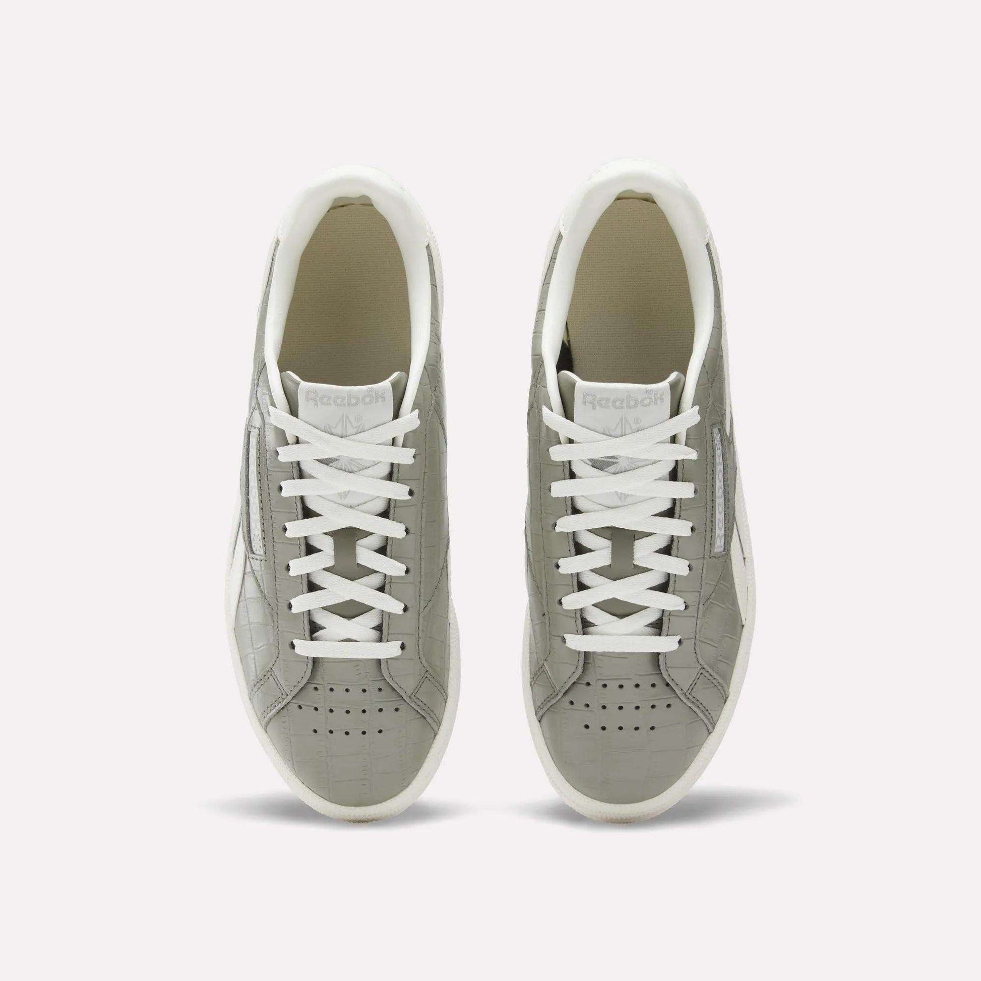A pair of Reebok Women's Club C Grounds UK shoes in grey with white laces and soles, shown from above on a plain white background. These court-inspired shoes have perforated toes and a clean white inner lining.