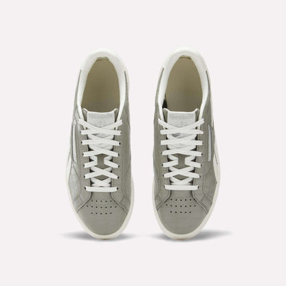 A pair of Reebok Women's Club C Grounds UK shoes in grey with white laces and soles, shown from above on a plain white background. These court-inspired shoes have perforated toes and a clean white inner lining.