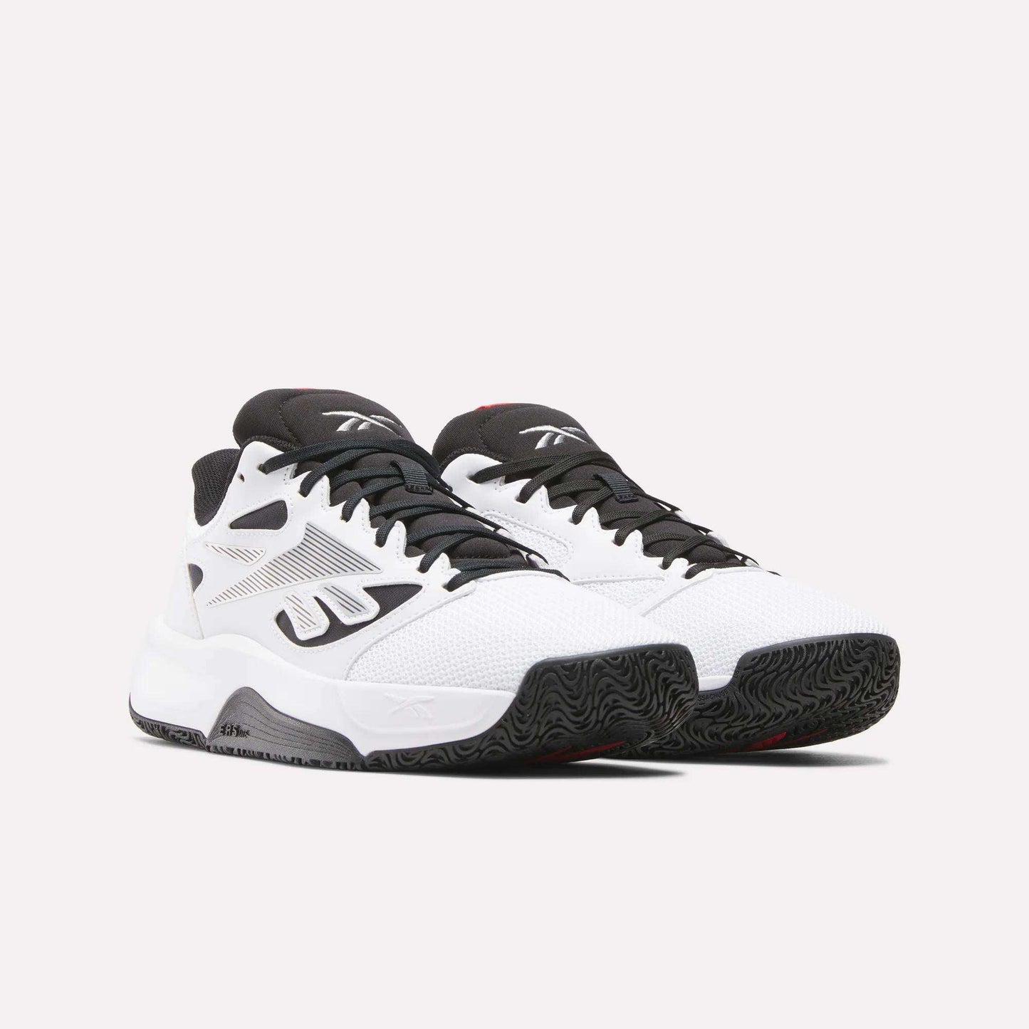 A pair of Reebok Engine LT Shoes in white with black accents and textured black soles, shown on a plain light background. These performance sneakers feature mesh uppers, the iconic logo, and a low-cut design for agility.