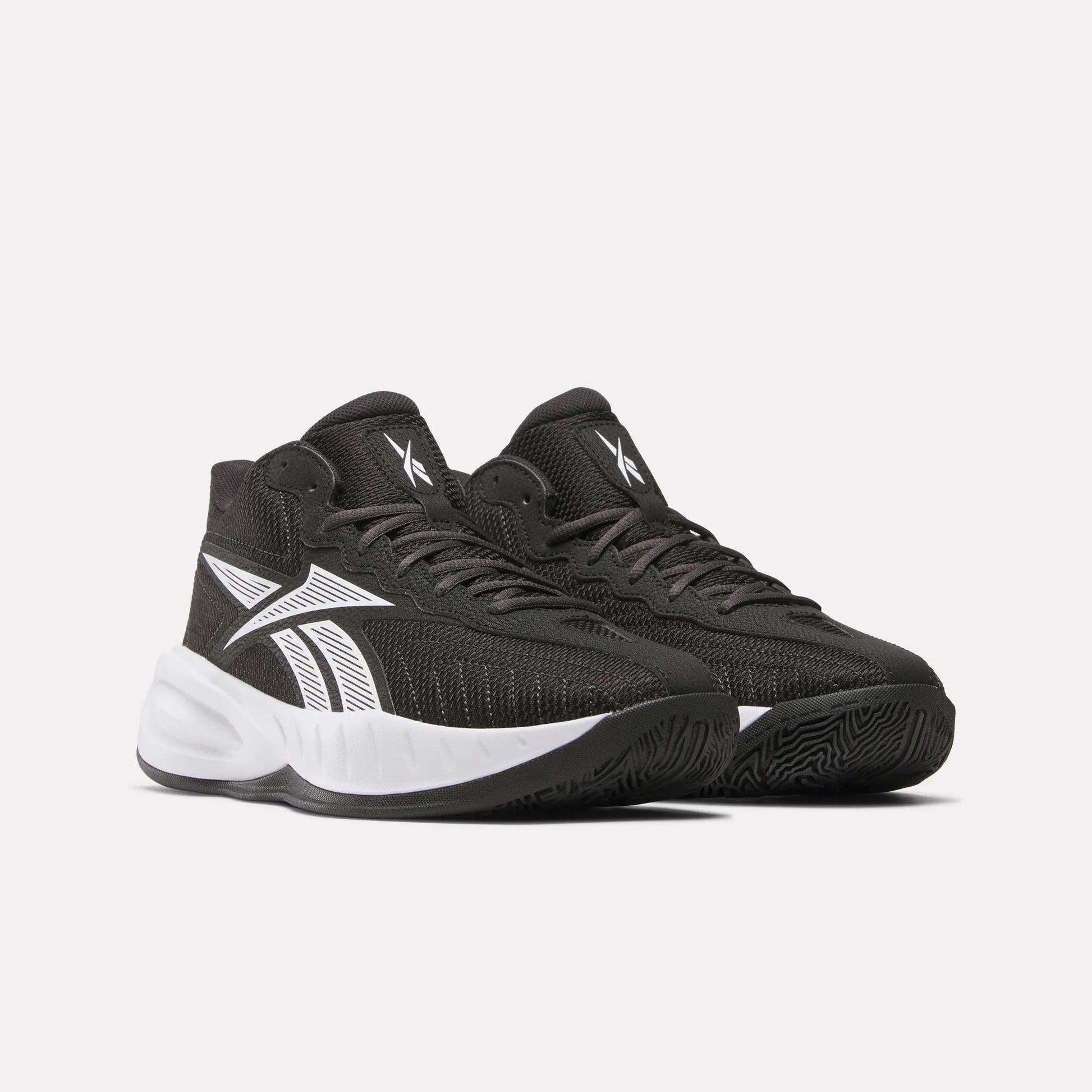 Reebok Press Basketball Shoes in black with white accents and soles, featuring a bold white side logo and EVA cushioning for comfort, are displayed against a plain light background.