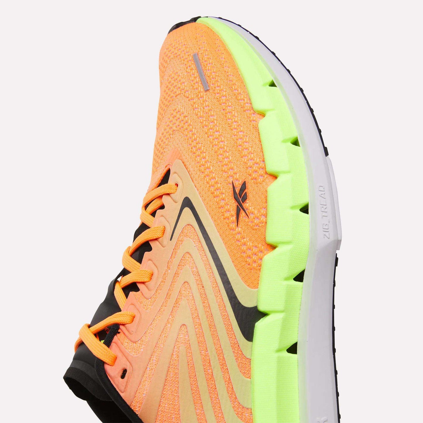 A close-up of Reebok Men's FloatZig Tread Running Shoes with an orange knit upper, black accents, and a bright green segmented sole. The cushioned midsole and wavy design offer comfort and style—ideal for treadmill workouts.