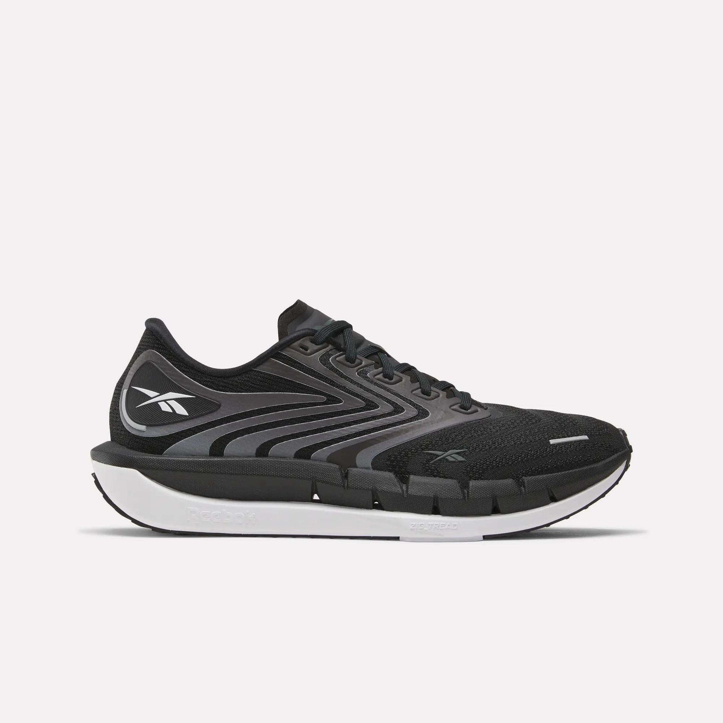 The Reebok Men's FloatZig Tread Running Shoes feature a black and gray design with a white sole, black laces, and a cushioned midsole, ideal for treadmill workouts. The Reebok logo is on the side against a plain white background.
