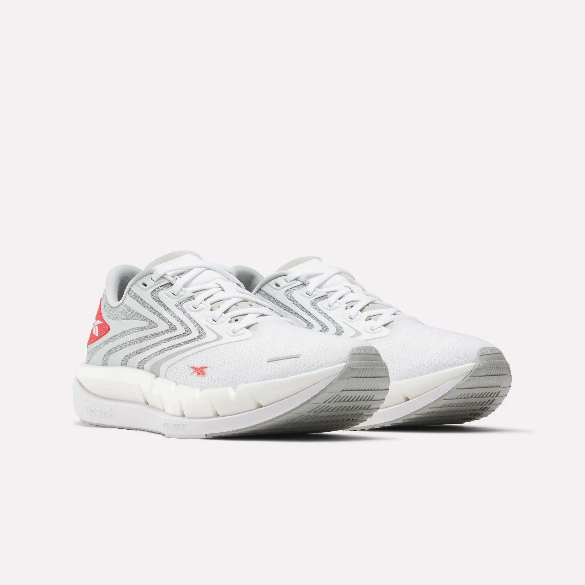 The Reebok Men's FloatZig Tread Running Shoes in white with light gray and red accents feature a zigzag side design, cushioned midsole, and textured sole—perfect for treadmill workouts—shown on a plain white background.