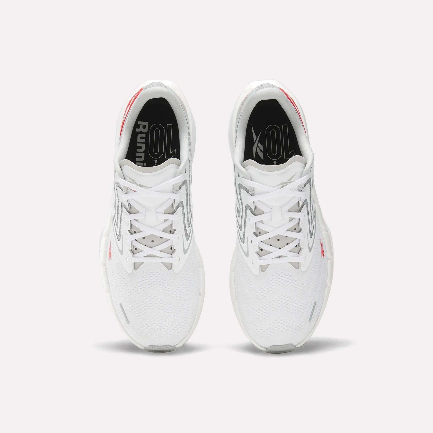 A pair of Men's FloatZig Tread Running Shoes by Reebok in white with gray and red accents, viewed from above, show the tops, laces, cushioned midsole, and "Running" text on black insoles—ideal for treadmill workouts.