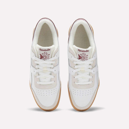 Top view of Reebok Workout Plus Shoes in white with gum soles, maroon Reebok logos on the tongues, and perforated toe boxes, evoking classic '80s fitness style against a light background.