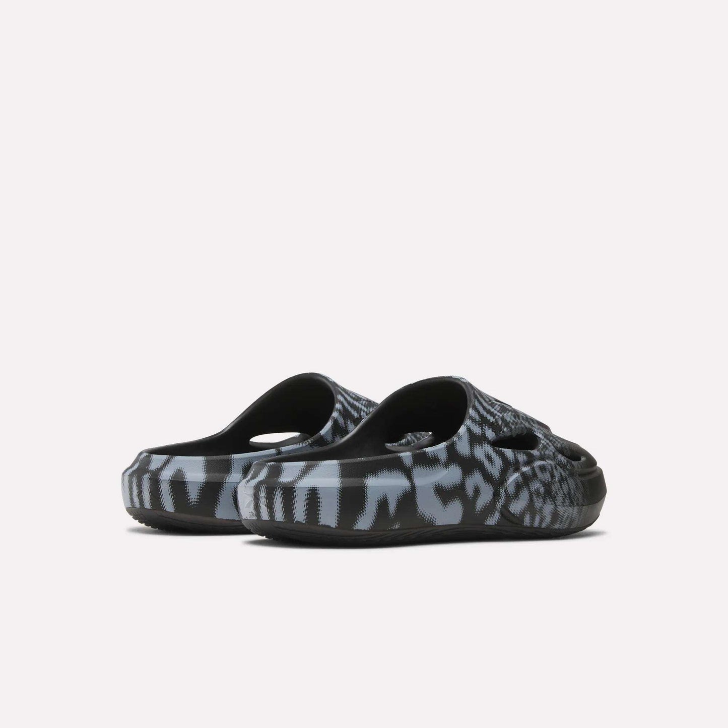 A pair of Reebok DMX Recovery Mules in black and grey with a bold animal print and DMX cushioning, shown from the back on a plain white background.