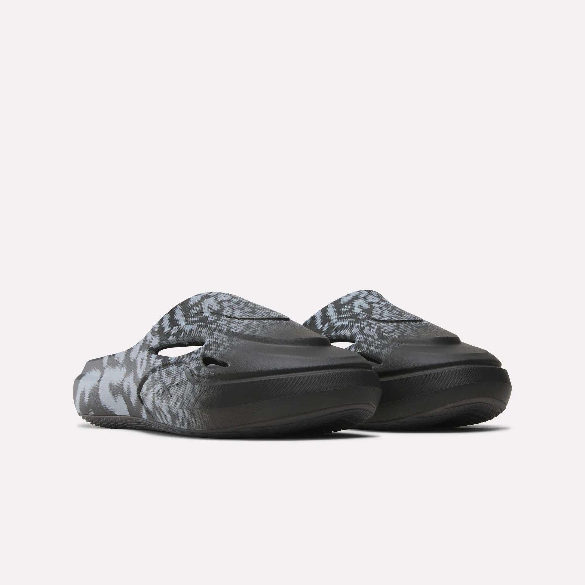 The Reebok DMX Recovery Mules feature a black and gray abstract, wavy pattern and DMX cushioning, shown on a light background from a low front angle.