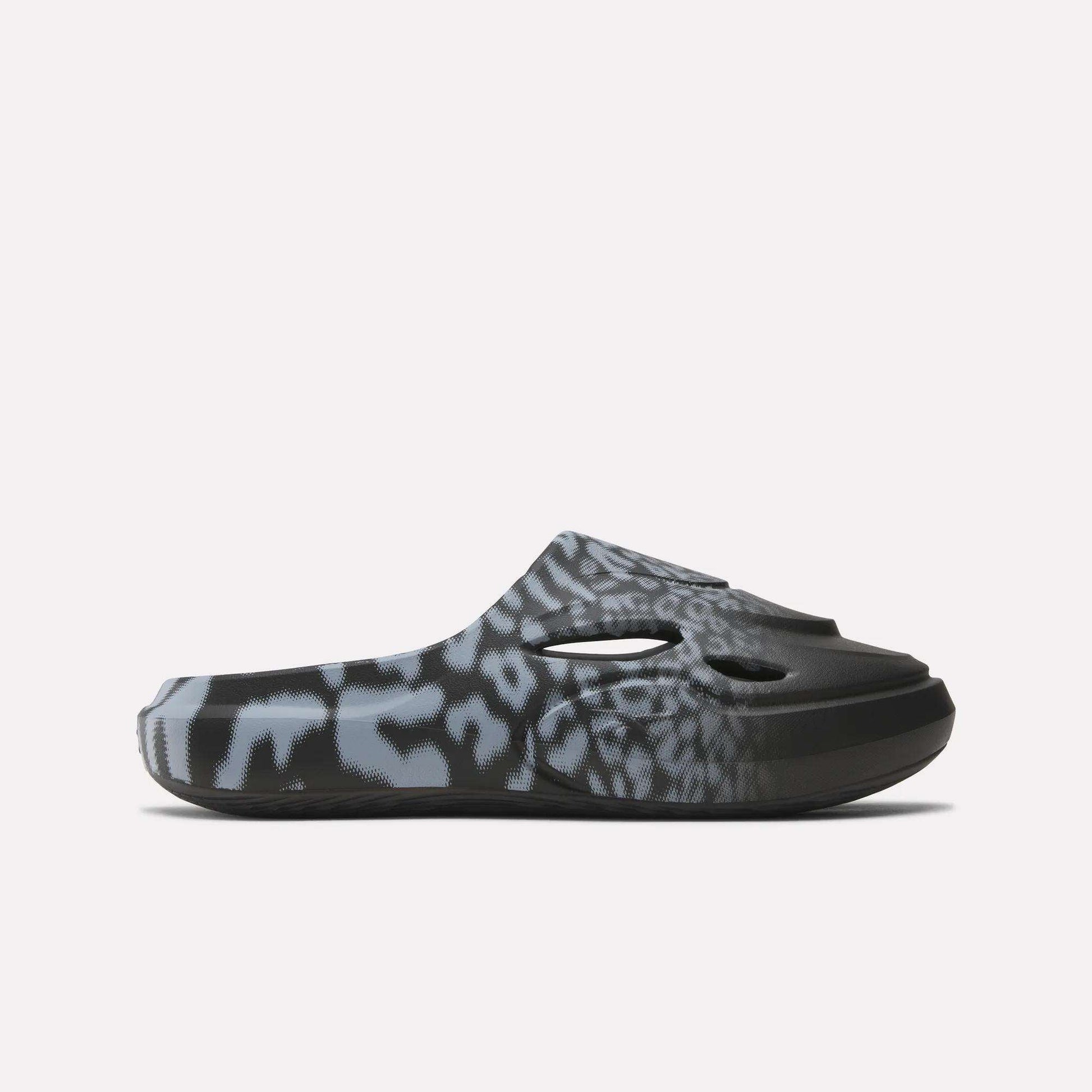 The Reebok DMX Recovery Mules are black slip-on clogs with ventilation holes and a blue-gray animal print, designed for recovery, shown in profile on a plain white background.