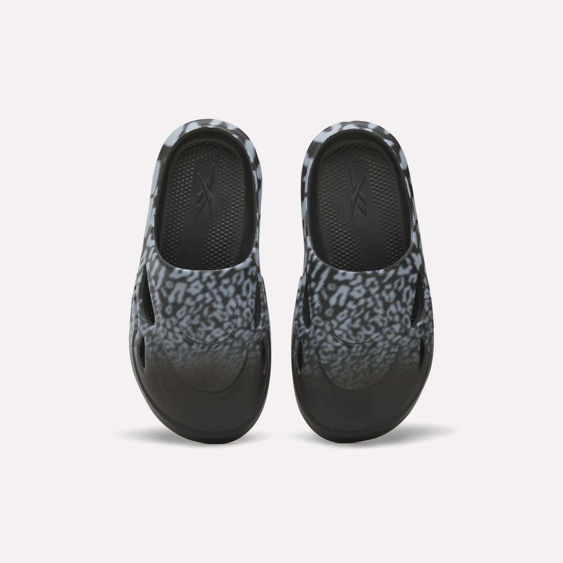 The Reebok DMX Recovery Mules feature a black and gray leopard print, shown from above on a white background—ideal recovery footwear after long days.