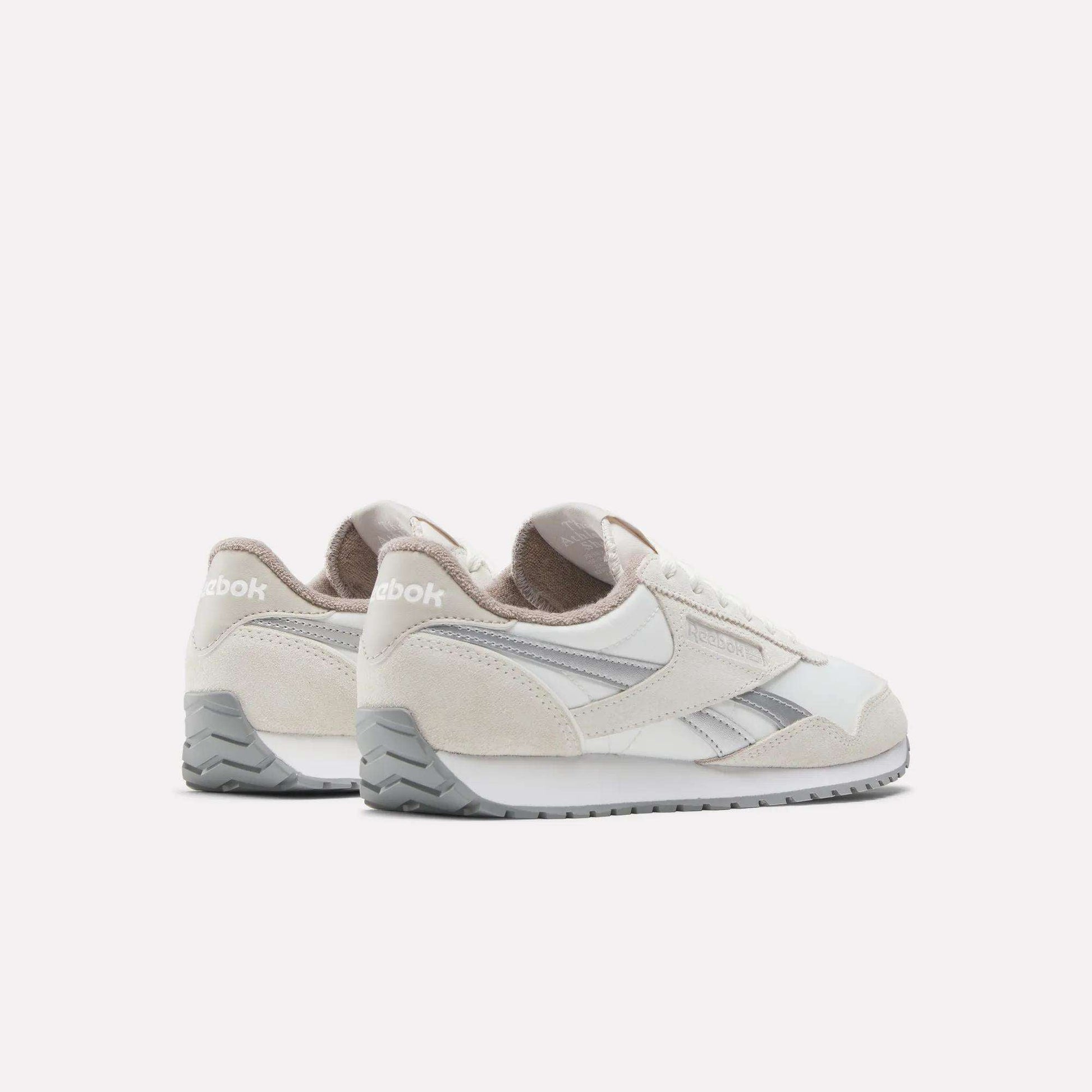 A pair of Reebok Women's Classic AZ Shoes in white and beige with gray accents are shown from a back-side angle, highlighting their timeless vintage style against a plain white background.