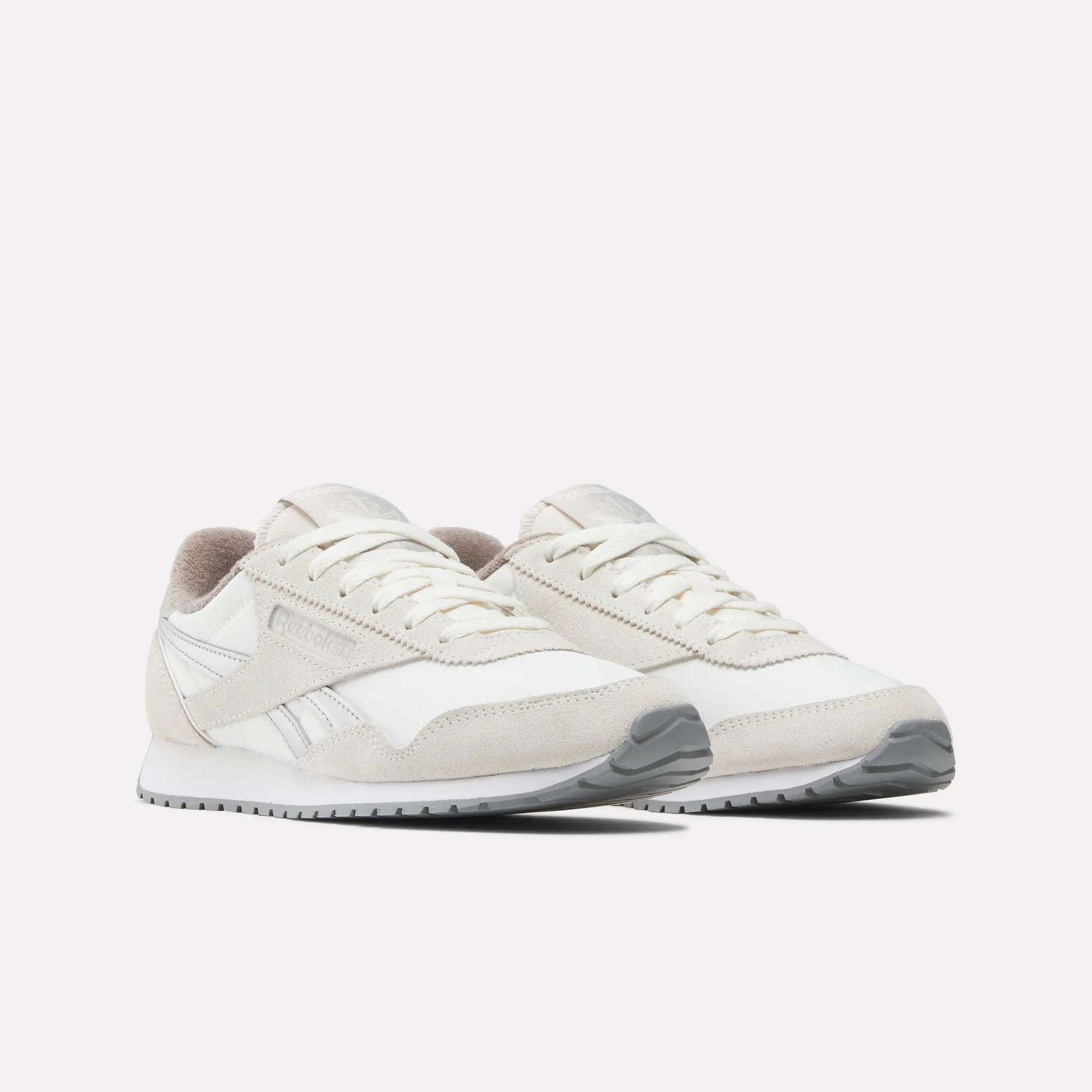 A pair of Reebok Women's Classic AZ Shoes in white and light beige with suede and mesh details, vintage-inspired accents, a low-cut design, white laces, and gray rubber soles displayed on a plain white background.